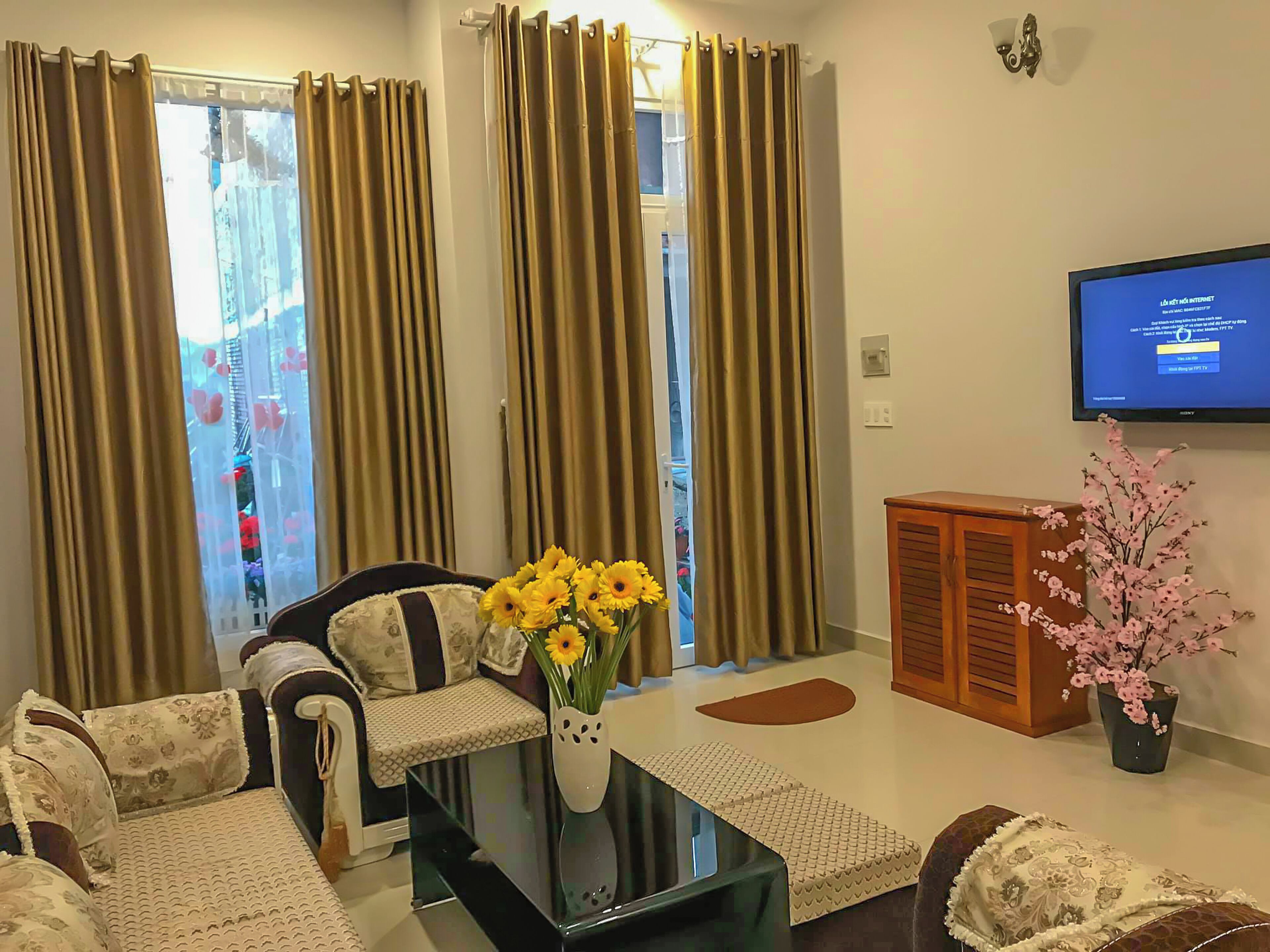 A living room with a sofa, a coffee table with a vase of flowers, a television, and a cabinet.