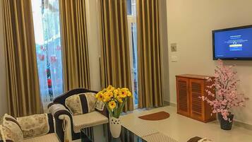 A living room with a sofa, a coffee table with a vase of flowers, a television, and a cabinet.