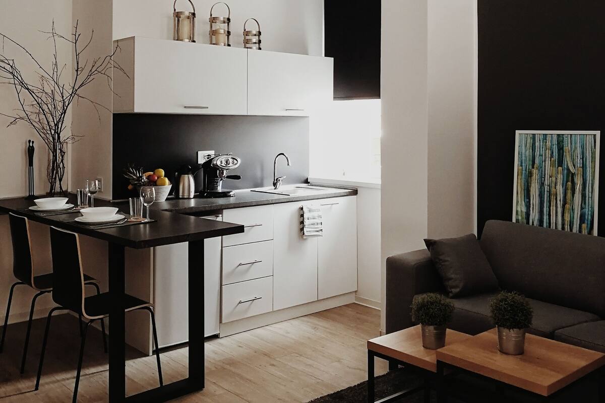 A modern kitchen with white cabinets, a black countertop, and a hanging pendant light.