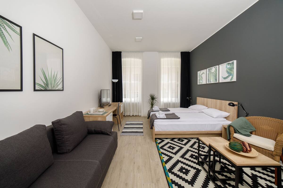 A modern hotel room with a bed, a sofa, a desk, and a dining area.
