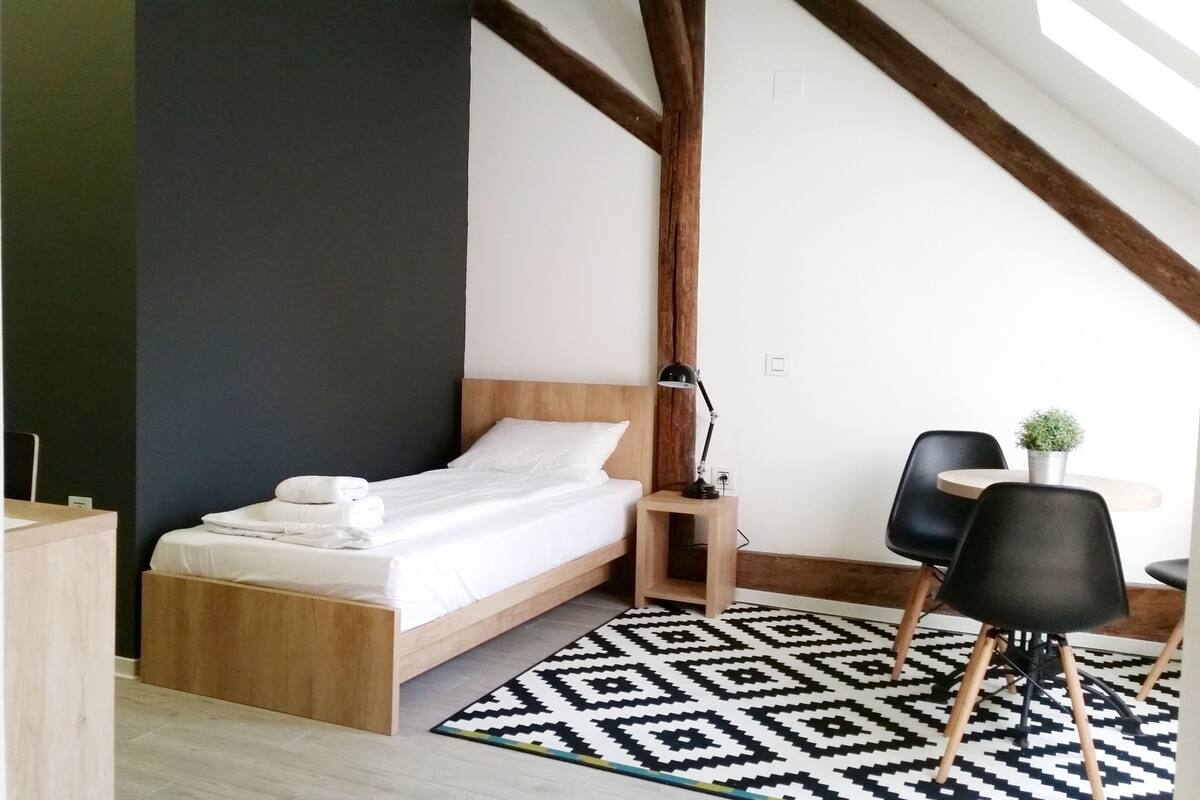 A modern bedroom with a wooden bed, a desk, a chair, and a small table with a plant.