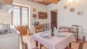 Zona de menjador amb mantell xatrat, cadires de fusta, cuina amb fogó i sostre rústic.