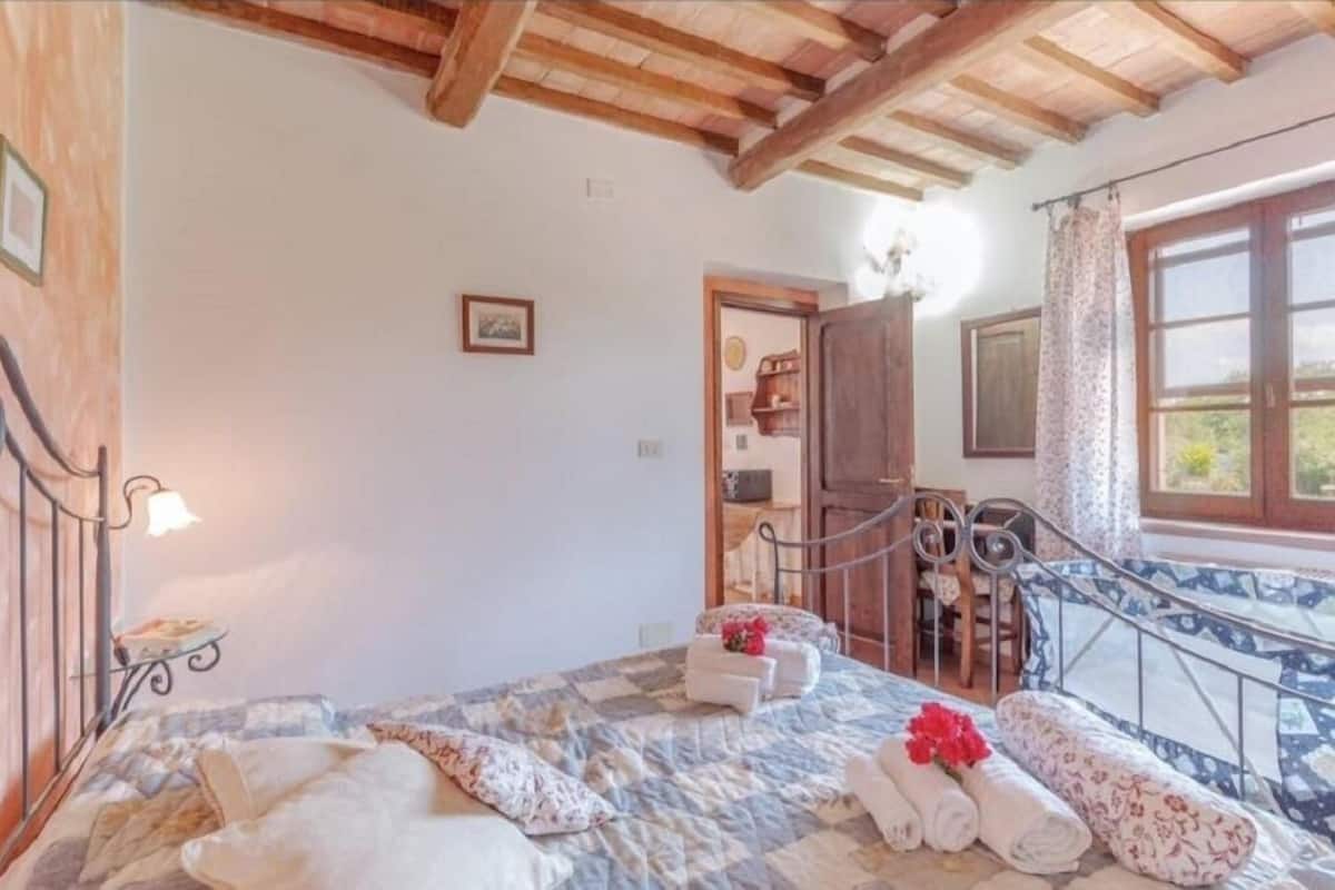 A bedroom with a bed, towels, a nightstand, a window, and a wooden ceiling.