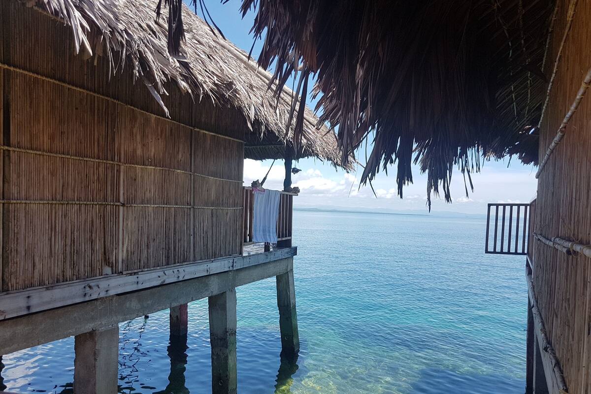 Una estructura de madera con techo de paja que da a aguas azules cristalinas.