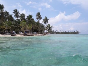 A beach with clear turquoise water, palm trees, and a small hut. - Cabanas Narasgandub - Naranjo Chico (Narganá)