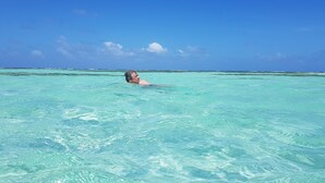 A person swimming in clear turquoise water with a distant horizon.