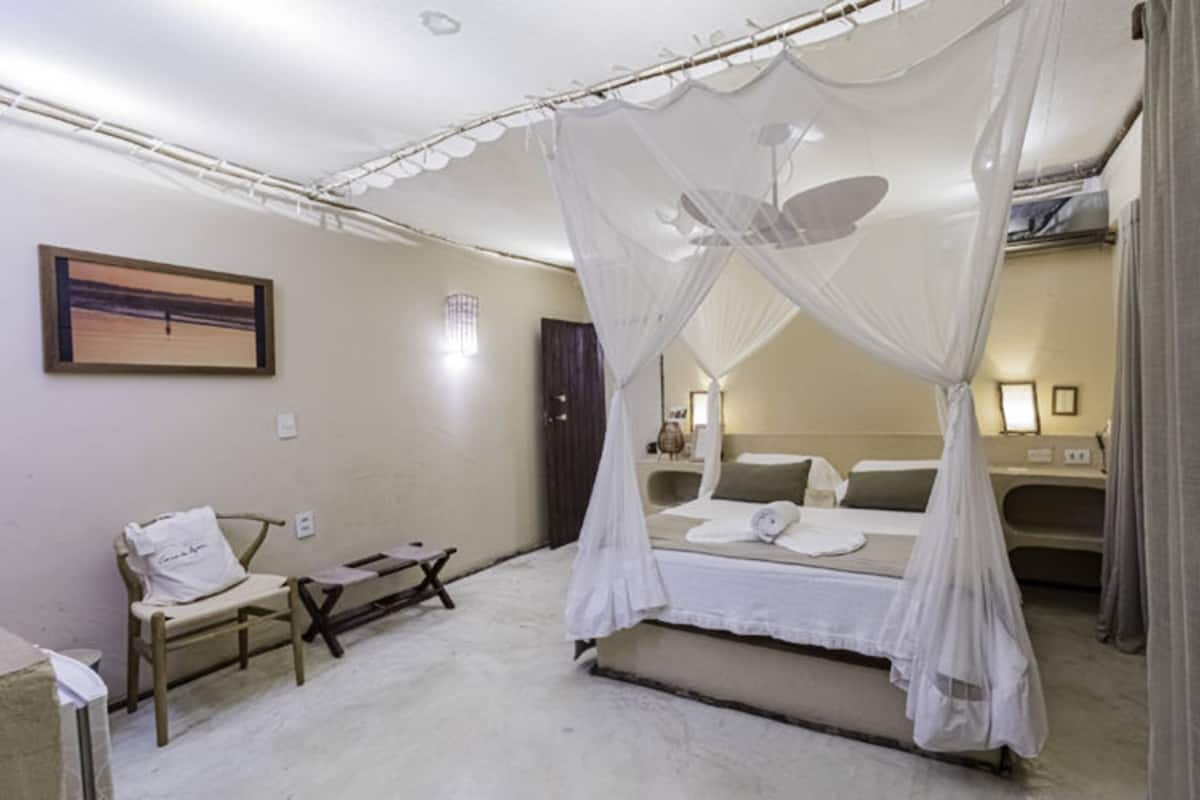 A bedroom with a four-poster bed, a bedside table, a chair, and a painting on the wall.