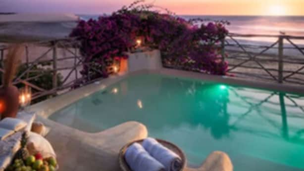 A poolside area with a view of the ocean at sunset, surrounded by a wooden deck and purple flowers. - Casa de Areia (Jijoca de Jericoacoara)