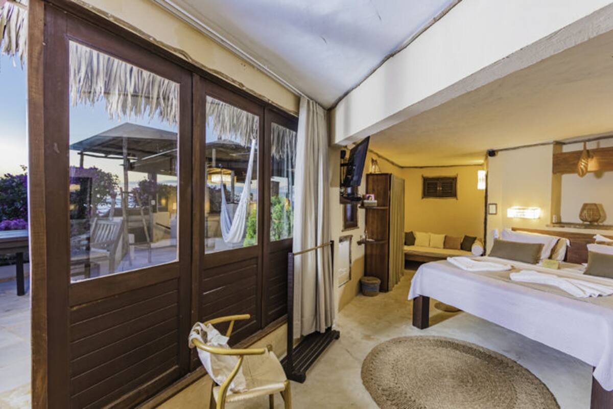 A hotel room with a bed, a chair, a small table, a mirror, and a view of the outside.