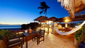 A patio with a wooden table and chairs, a hammock, and a thatched roof structure overlooking the ocean. - Casa de Areia (Jijoca de Jericoacoara)