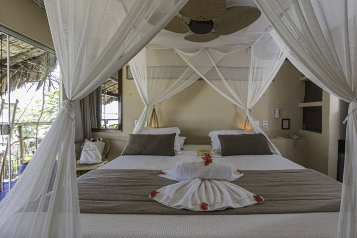 A room with a bed under a canopy, two bedside tables, and a window with a view of greenery.