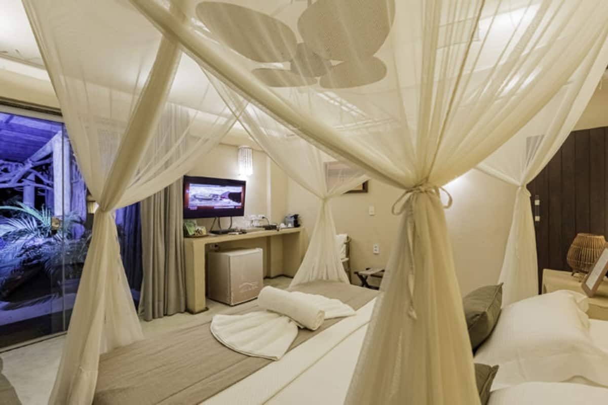 A room with a bed, a desk, a TV, and a view of a tropical landscape.
