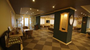 A hotel lobby with checkered flooring, multiple seating areas, a reception desk, and a wall-mounted television. - Aykut Palace Otel (Iskenderun)