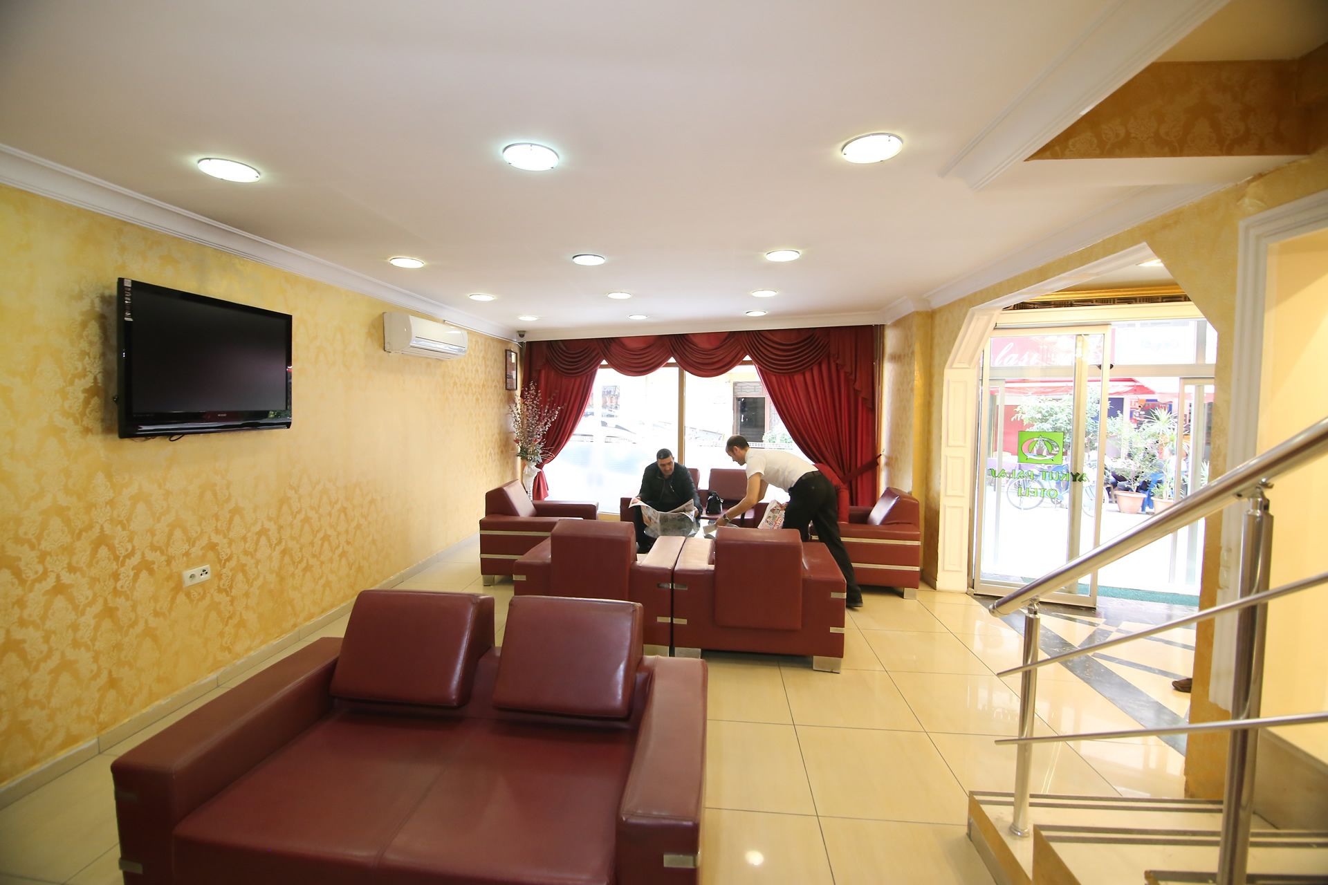 A hotel lobby with a TV mounted on the wall, a staircase, and a seating area with red sofas.