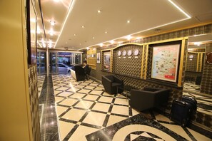 A hotel lobby with a checkered floor, a reception desk, a seating area, and a wall with a map and clocks. - Aykut Palace Otel (Iskenderun)