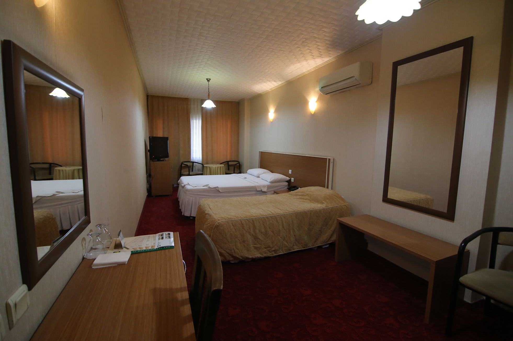 Une chambre d’hôtel avec deux lits, un bureau, une chaise, un miroir et un téléviseur.