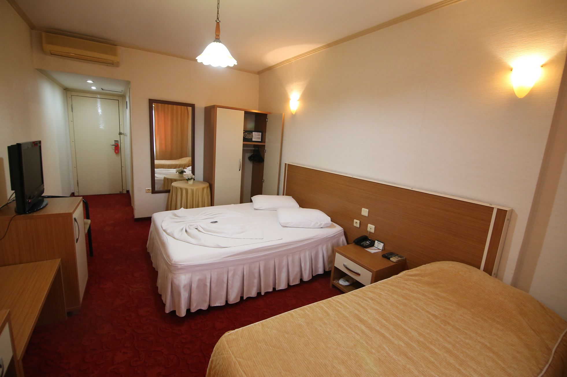 Una habitación de hotel con cama, escritorio, silla, televisión, espejo y armario.