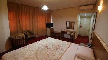 Habitación de hotel con una cama grande, un escritorio, una silla, un televisor y una puerta.
