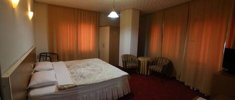 A hotel room with a bed, a desk, a chair, a TV, and a red carpet.