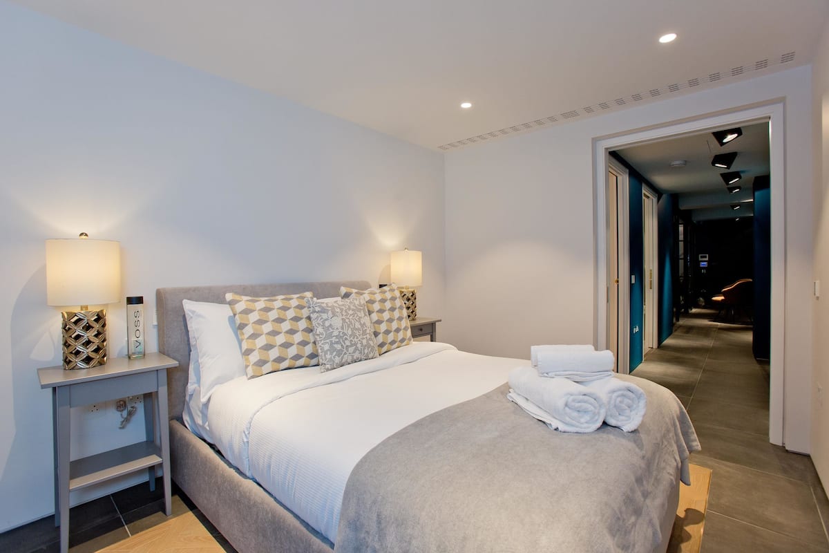 Una habitación de hotel moderna con una cama bien hecha, dos lámparas de noche y una puerta de baño visible.
