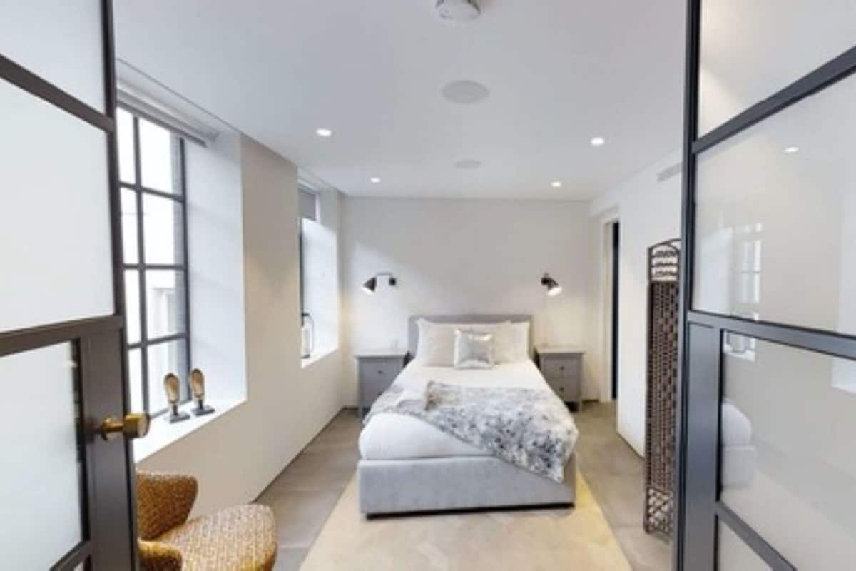 Un dormitorio moderno con una cama grande, mesitas de noche, una silla y un ventanal.