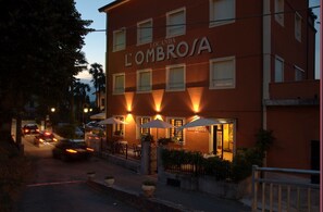 A building with the sign 'LOMBROSA' and 'RISTORANTE BAR' indicating a restaurant bar. There are outdoor seating areas with umbrellas and potted plants. - Hotel Locanda l'Ombrosa (Vezzano Ligure)