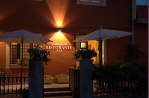 An outdoor entrance to L'Ombrosa Ristorante Bar with a warm light, potted plants, and a metal gate. - Hotel Locanda l'Ombrosa (Vezzano Ligure)