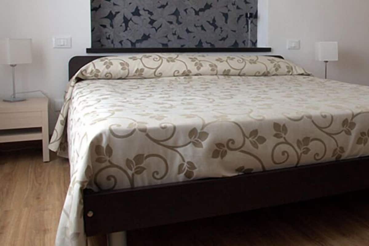 A neatly made bed with a floral bedspread, a wooden nightstand with a lamp, and a wooden wardrobe in a hotel room.
