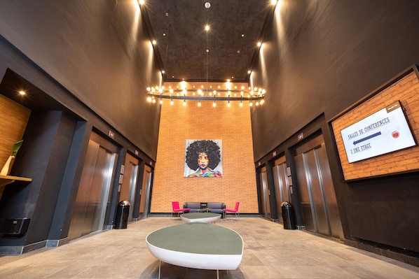 A modern lobby with a central seating area, a large mural on the back wall, and a sign indicating the conference rooms.