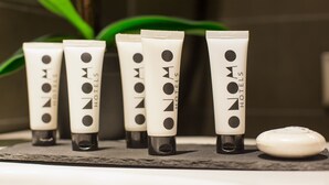 Five tubes of hotel toiletries on a shelf with a soap bar beside them.