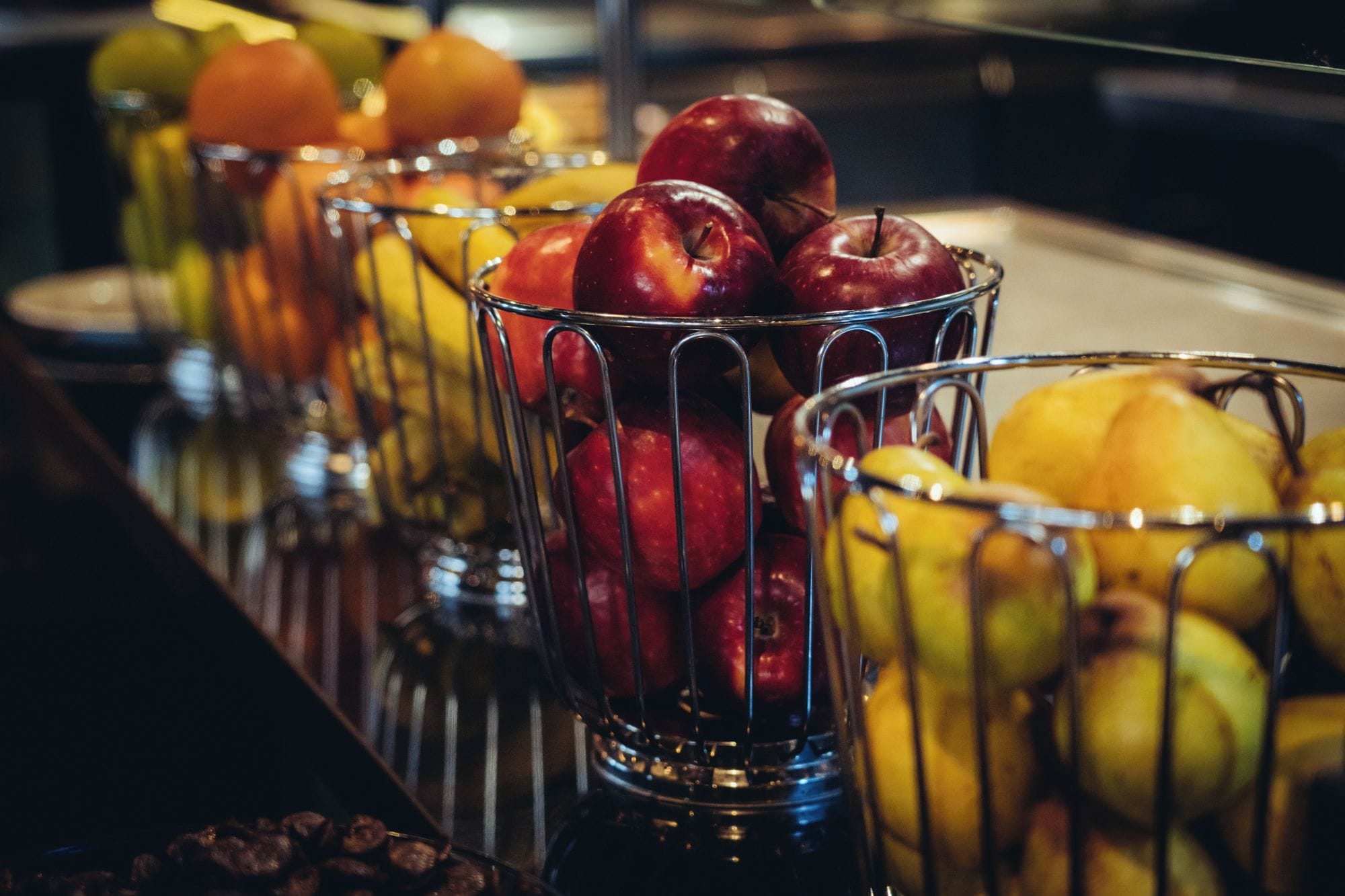 A row of metal baskets filled with various fruits.