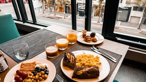 A breakfast table with plates of food, glasses of orange juice, and a view of the city through large windows. - ONOMO Hotel Casablanca City Center (Casablanca)