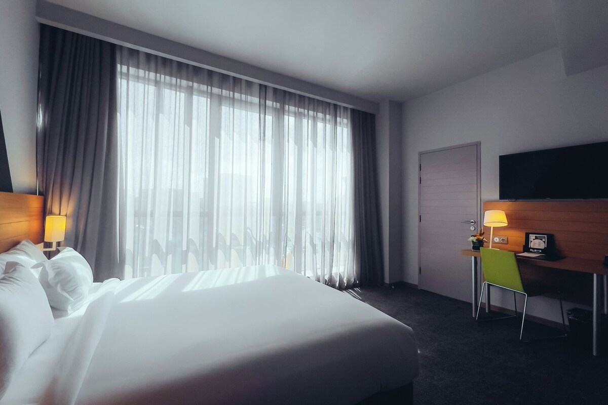 Habitación de hotel con una cama grande, un escritorio con silla, un televisor montado en la pared y una puerta.