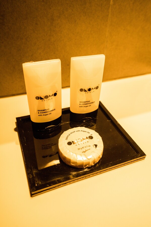 Dos botellas de champú y acondicionador de Onoma Hotels con aceite de argán, y una barra de jabón suave de Onoma Hotels con aceite de argán sobre una bandeja negra.