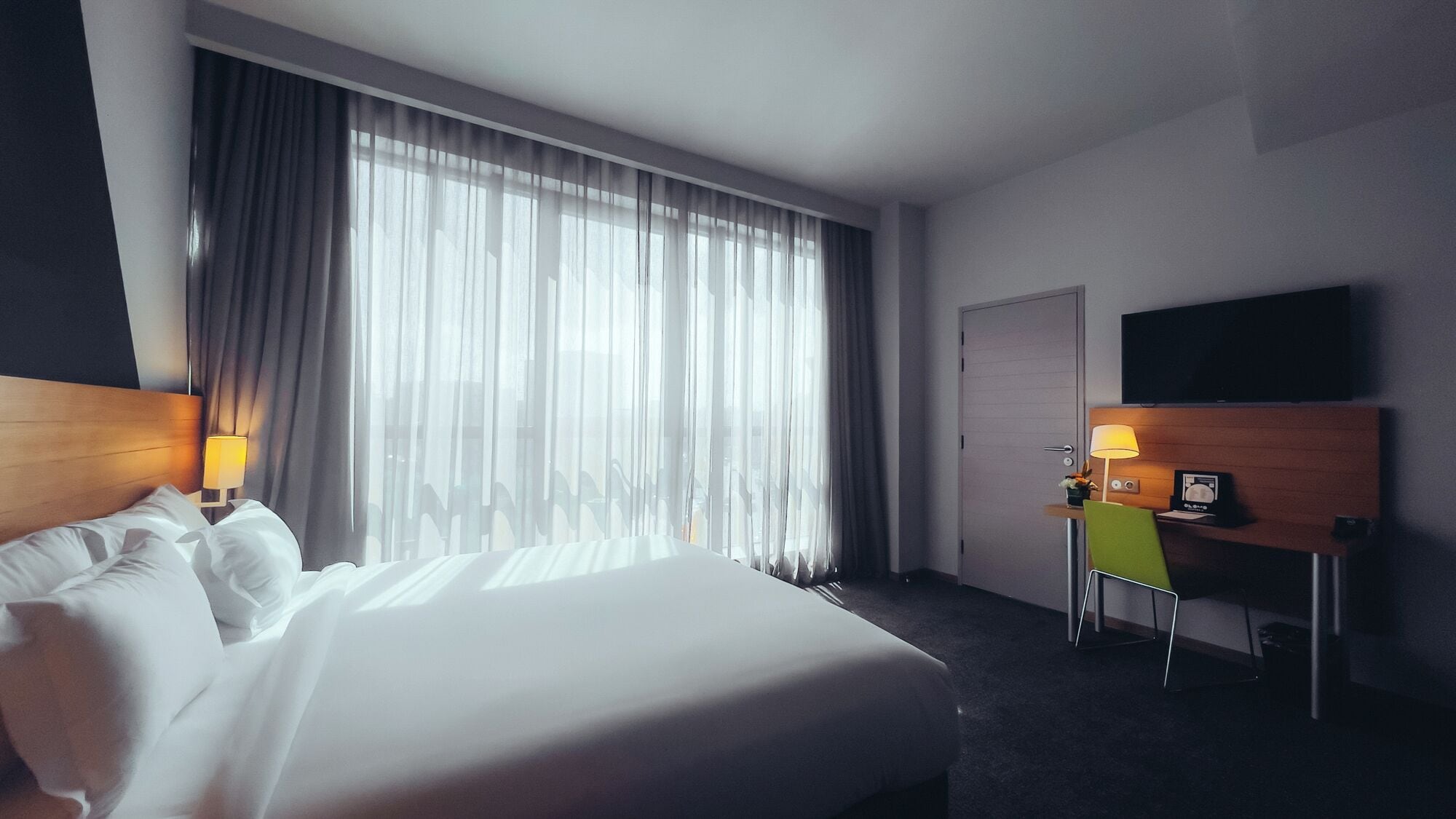 Une chambre d’hôtel avec un grand lit, un bureau avec une chaise, un téléviseur fixé au mur et une porte.