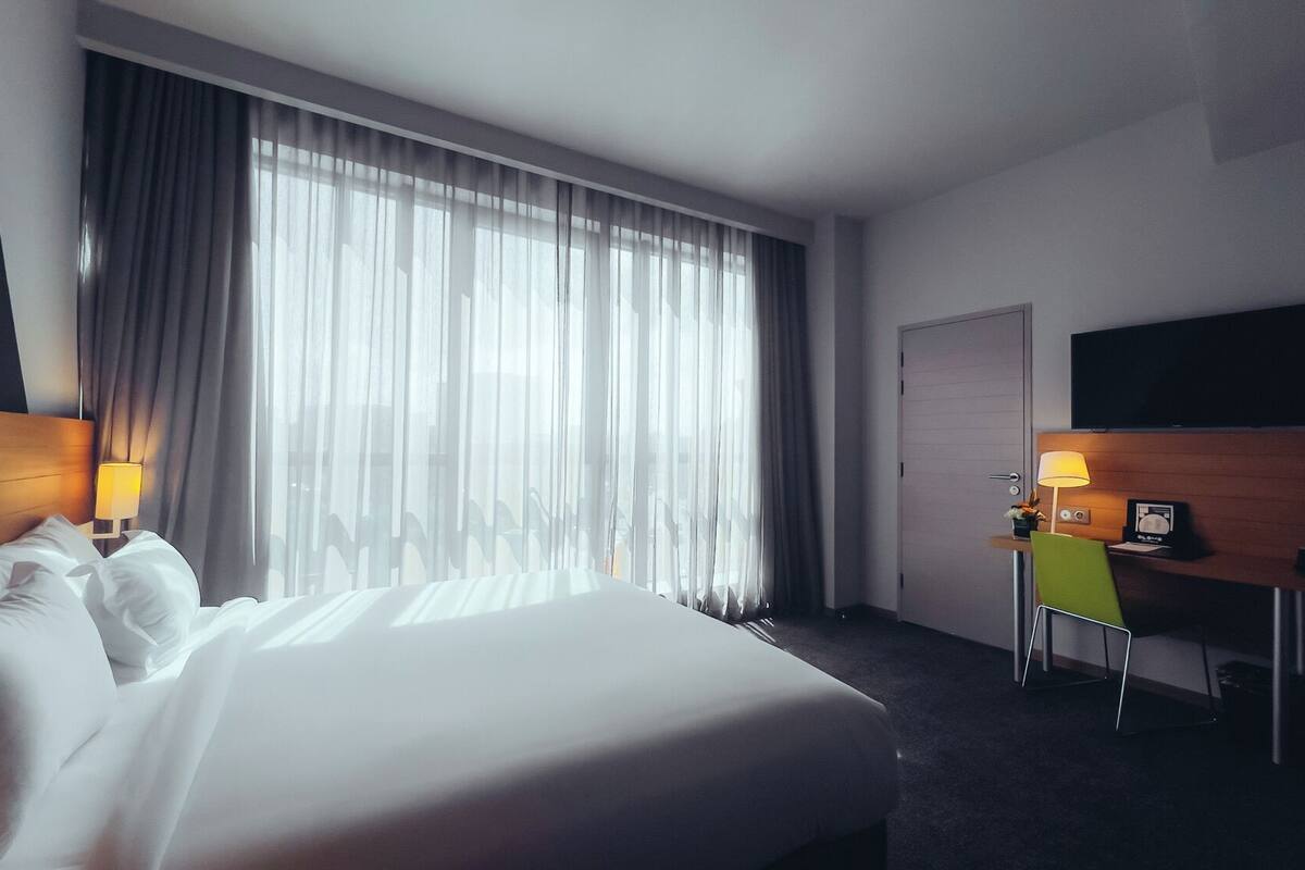 Une chambre d’hôtel avec un grand lit, un bureau avec une chaise, un téléviseur fixé au mur et une porte.