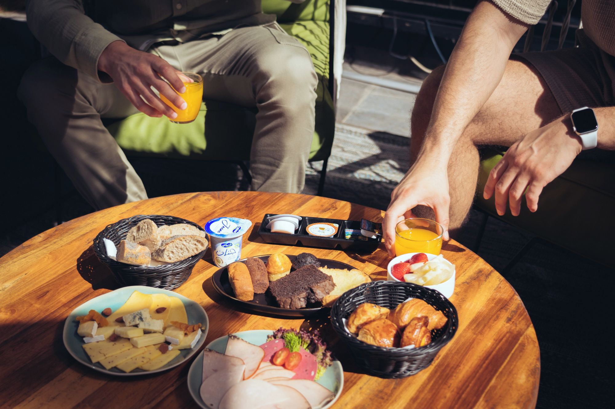 Une table ronde en bois, sur laquelle sont disposés divers aliments et boissons, notamment du pain, du fromage et un verre de jus d’orange.