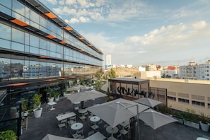 Terraza en la azotea con mobiliario exterior, plantas en macetas y vistas de la ciudad.