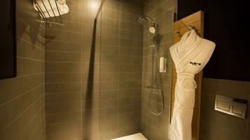 A modern bathroom with a glass-enclosed shower, a wooden vanity, and a robe hanging on the wall.