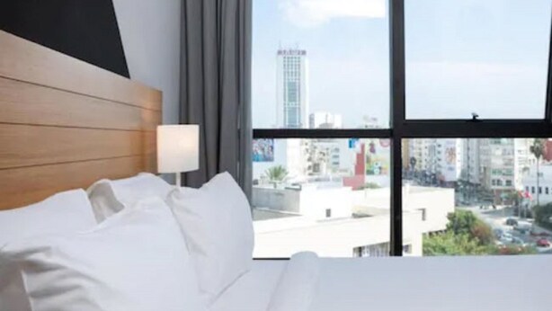 A hotel room with a bed, a window with a city view, and a modern design.