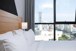 Habitación de hotel con cama, ventana y vista a la ciudad, con un diseño moderno.