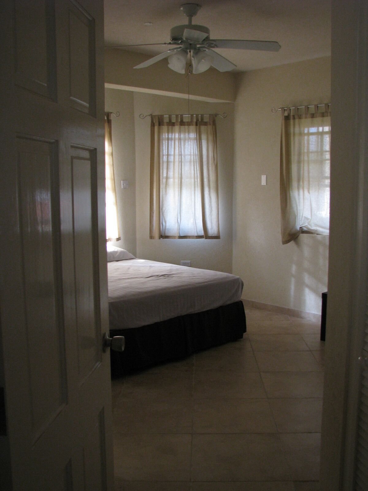 A bedroom with a bed, a ceiling fan, and a window with curtains.