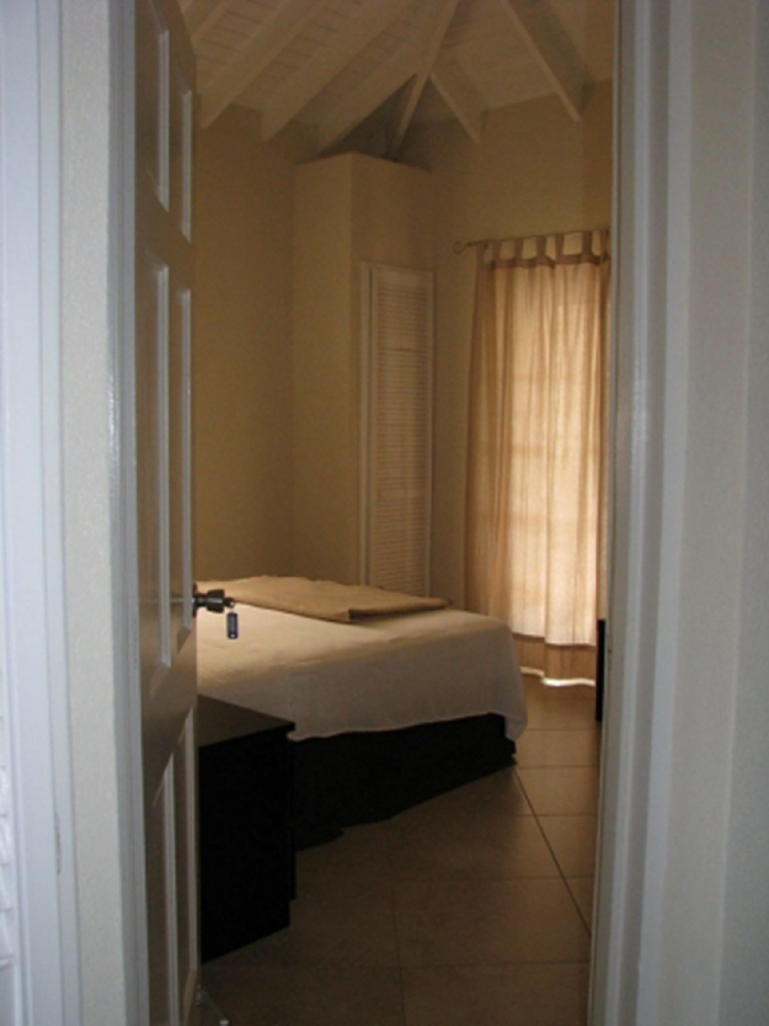 A bedroom with a bed, a nightstand, a window with curtains, and a door.