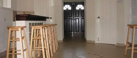 Un pasillo con una fila de taburetes de madera, una puerta blanca y una puerta negra con paneles de vidrio.