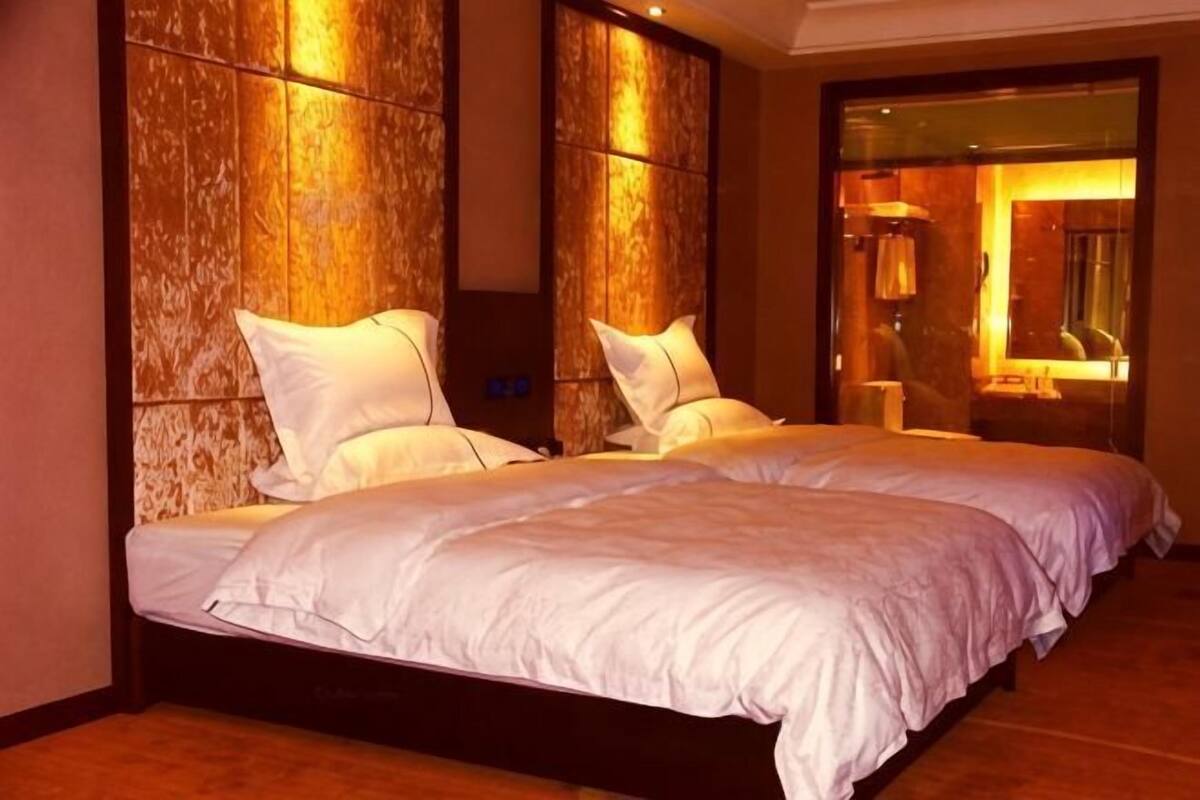 A double bed with white bedding, a wooden headboard, and a mirror reflecting a room with a lamp.