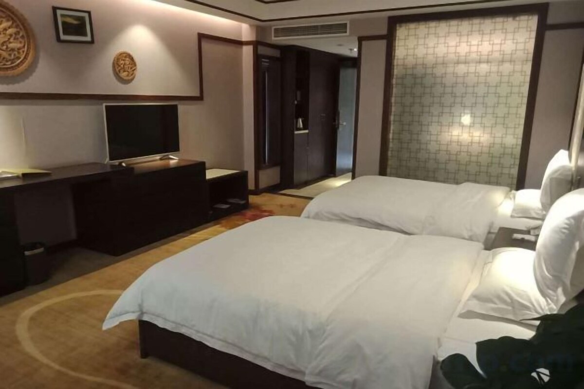 Een hotelkamer met twee bedden, een televisie, een bureau en een groot raam.