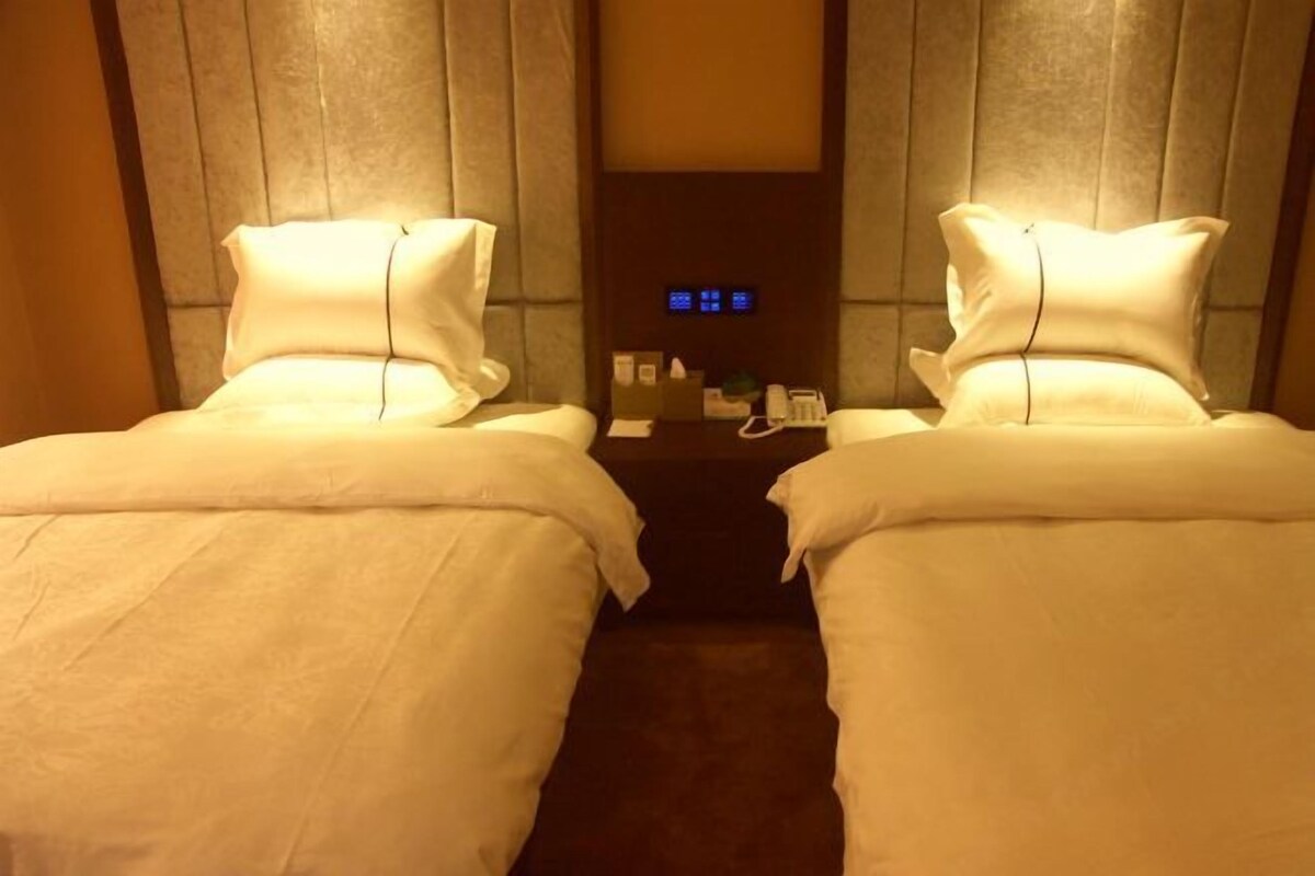 A hotel room with two beds, a control panel, and a small table with amenities.