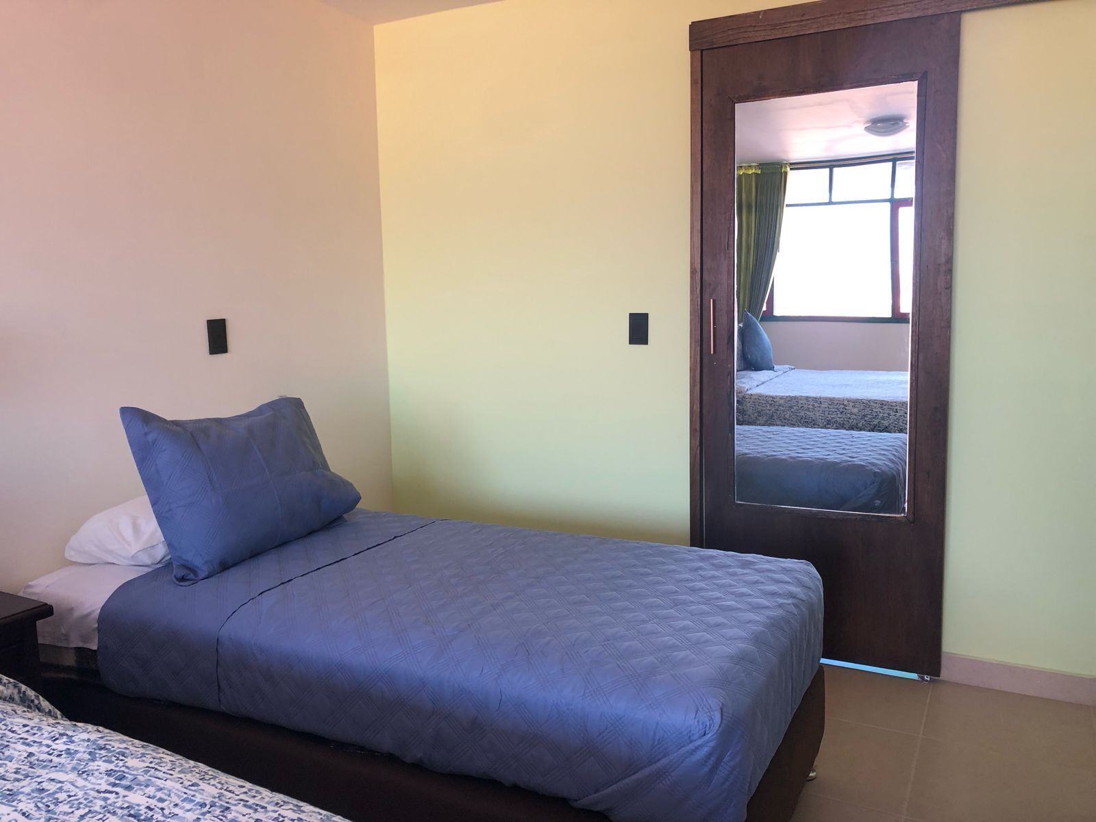 Un dormitorio con cama, mesita de noche, espejo y una puerta que da a otra habitación.