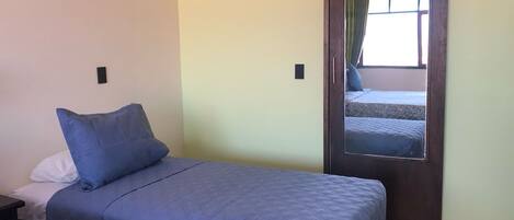 Un dormitorio con cama, mesita de noche, espejo y una puerta que da a otra habitación.