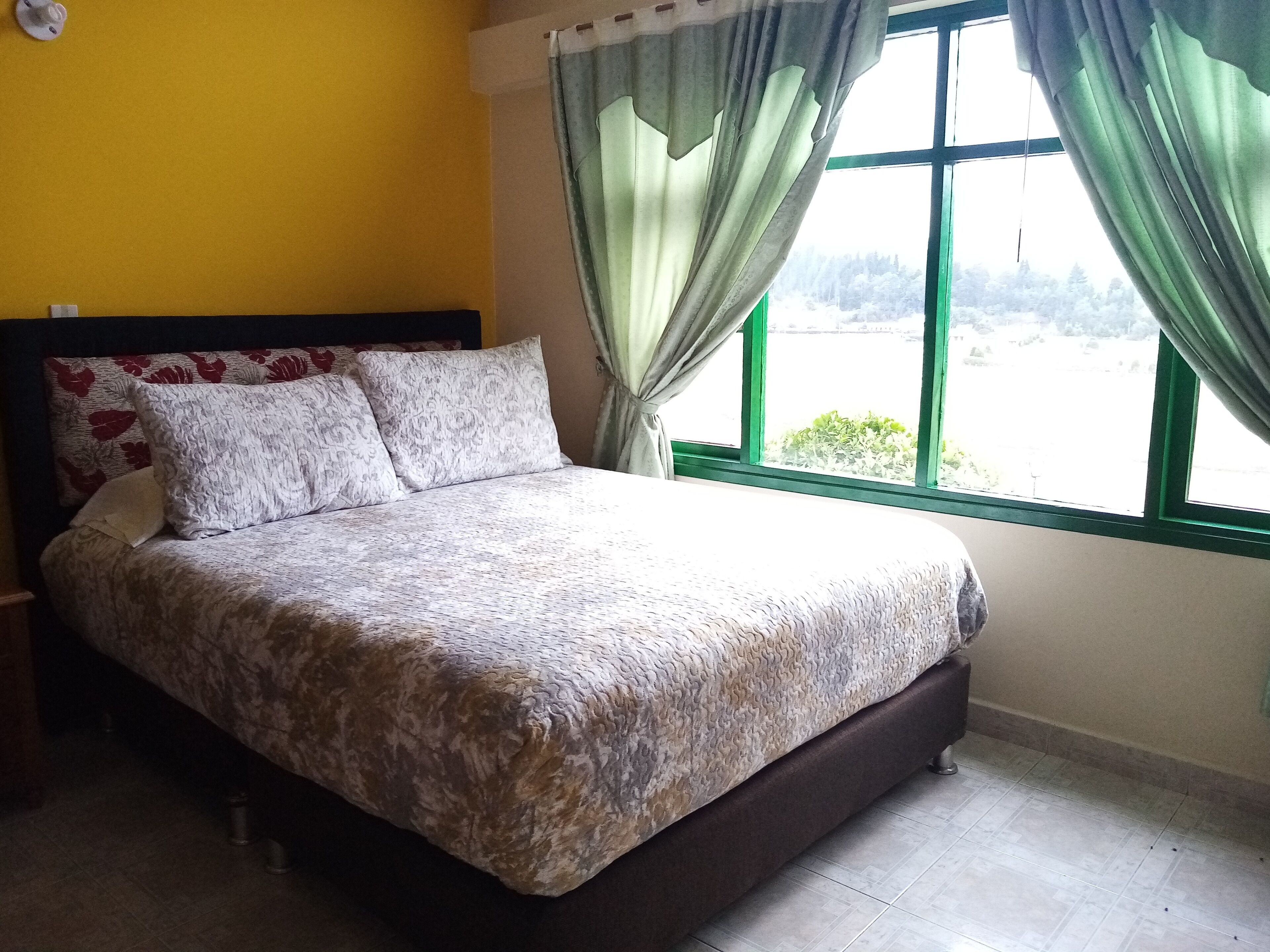 Una cama con ropa de cama estampada, un cabecero con diseños florales y una ventana con cortinas.